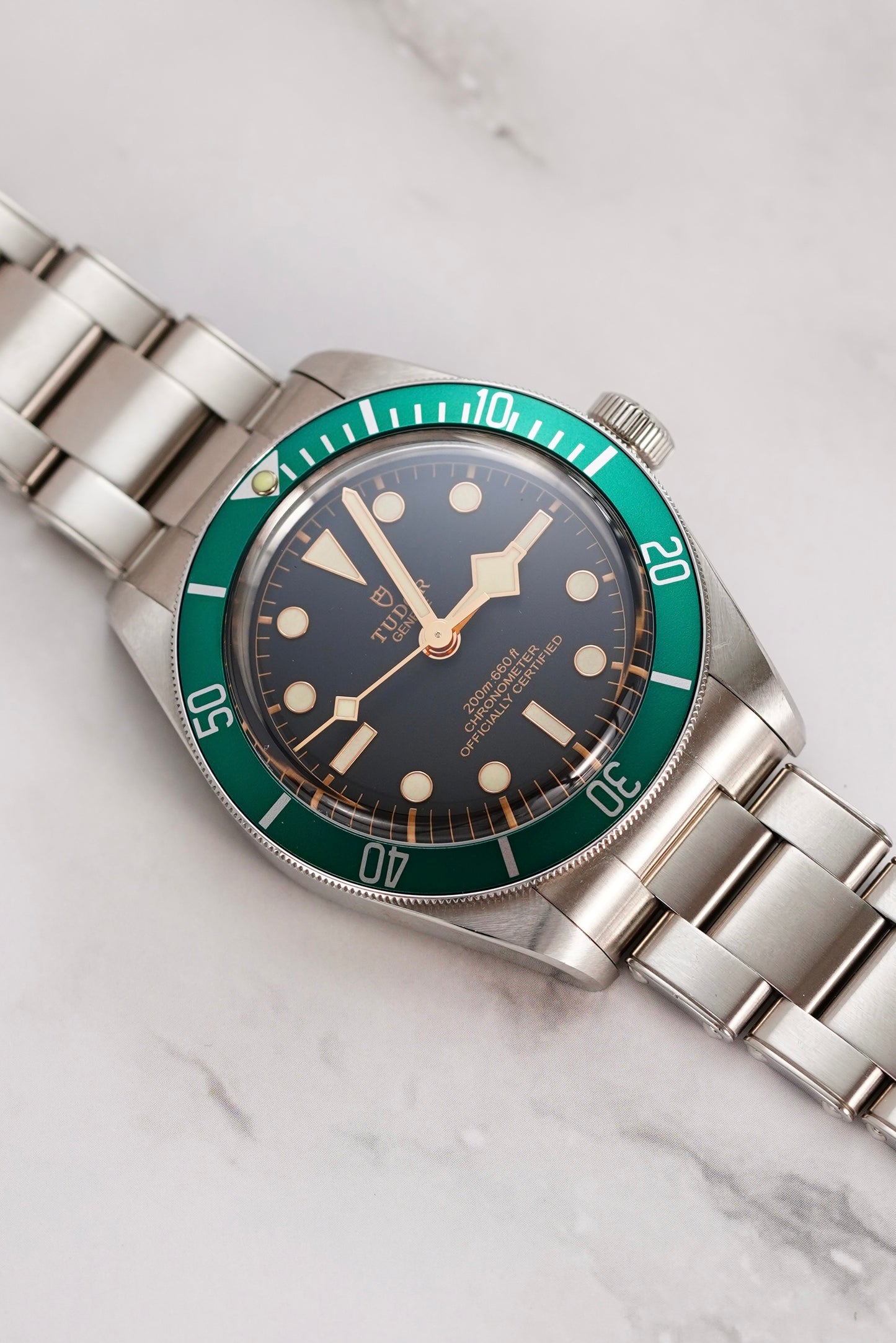 Watch with green bezel and silver bracelet on a marble background