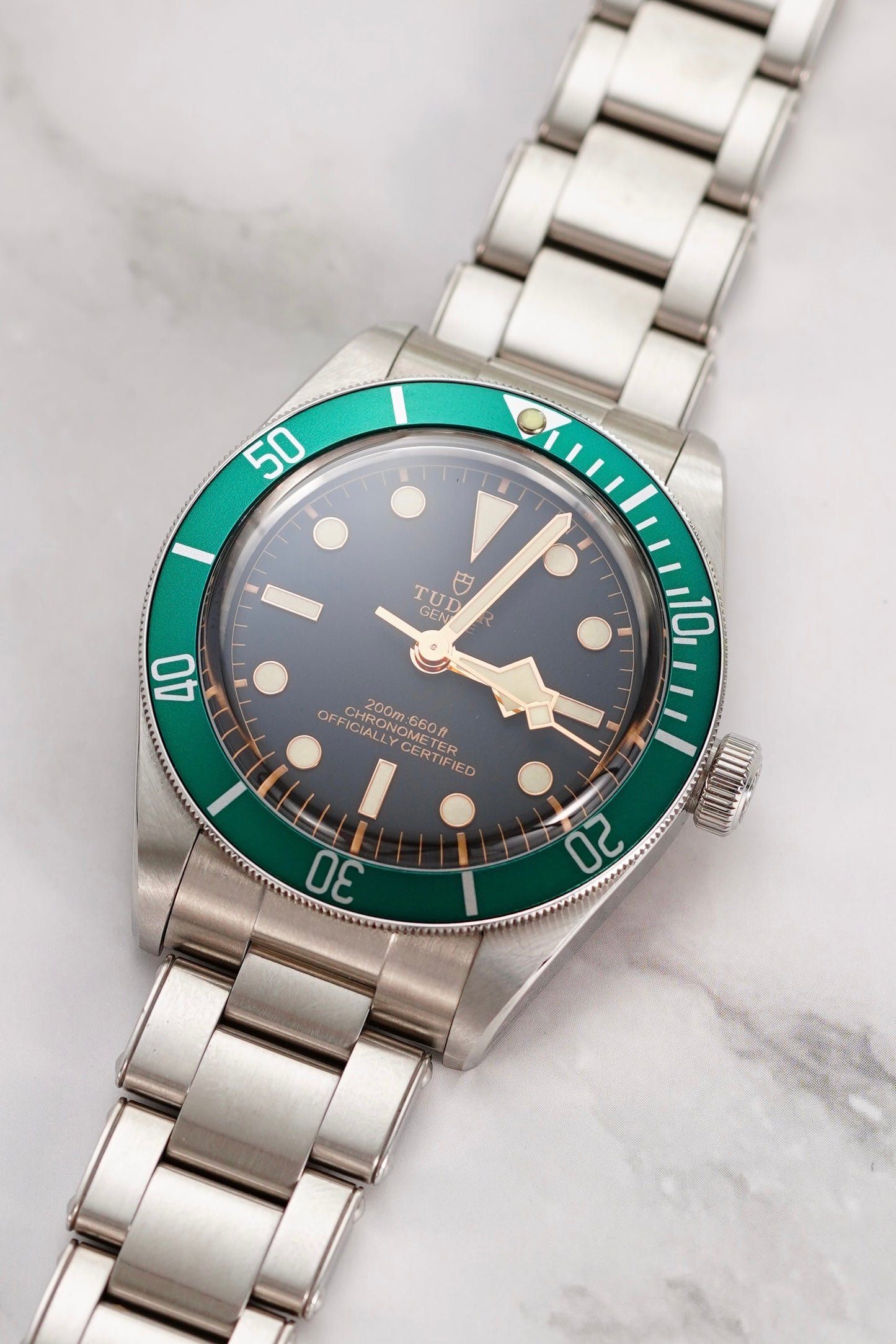 Watch with silver bracelet and green bezel on a marble surface