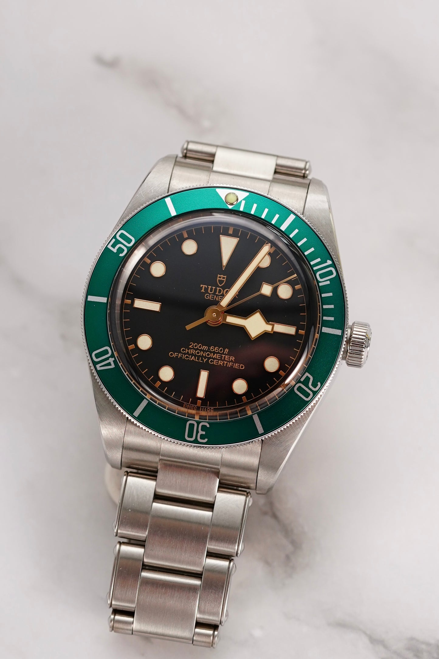 Silver watch with a green bezel and black face on a light gray background