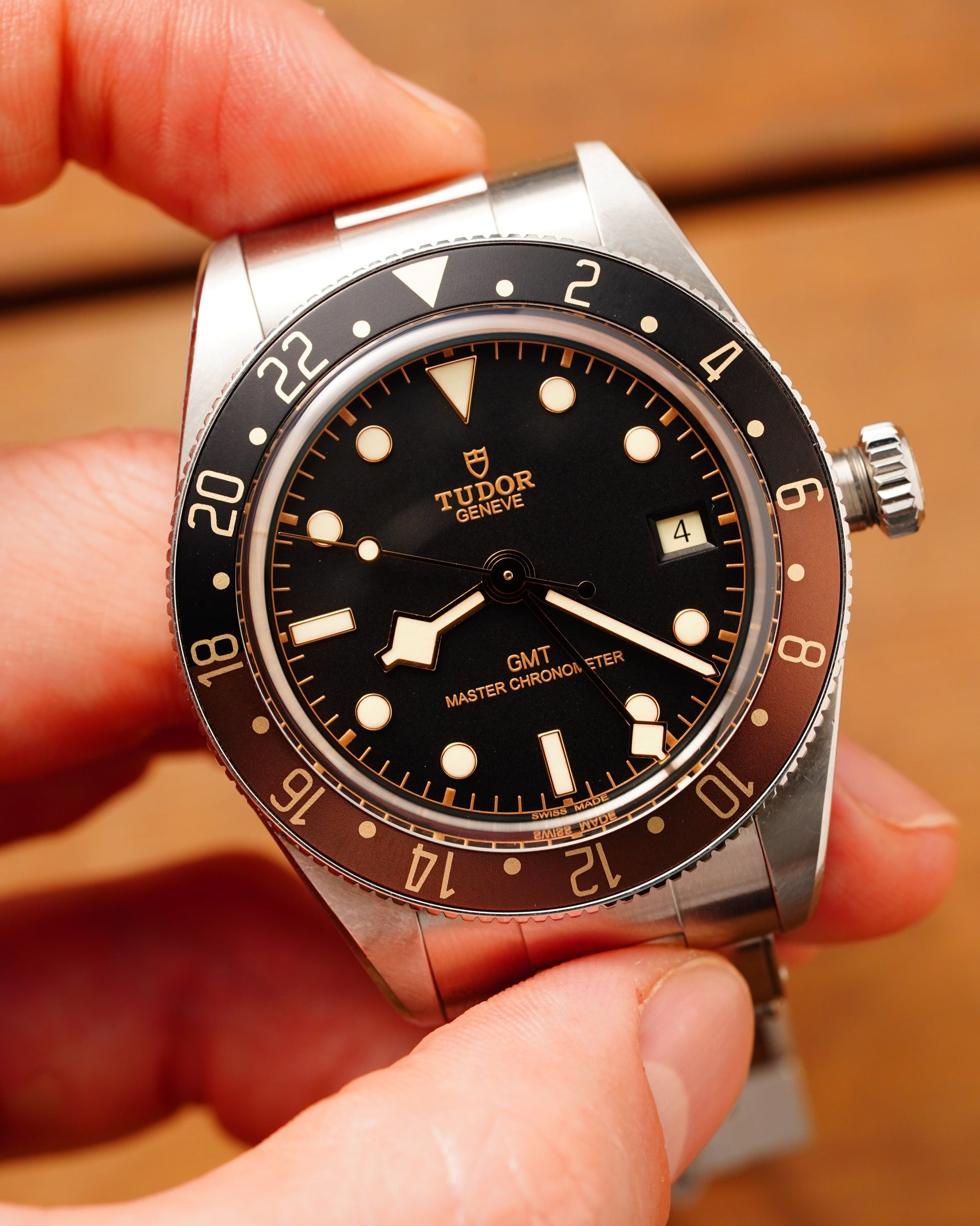 Close-up of a Tudor watch held in a hand with a blurred wooden background