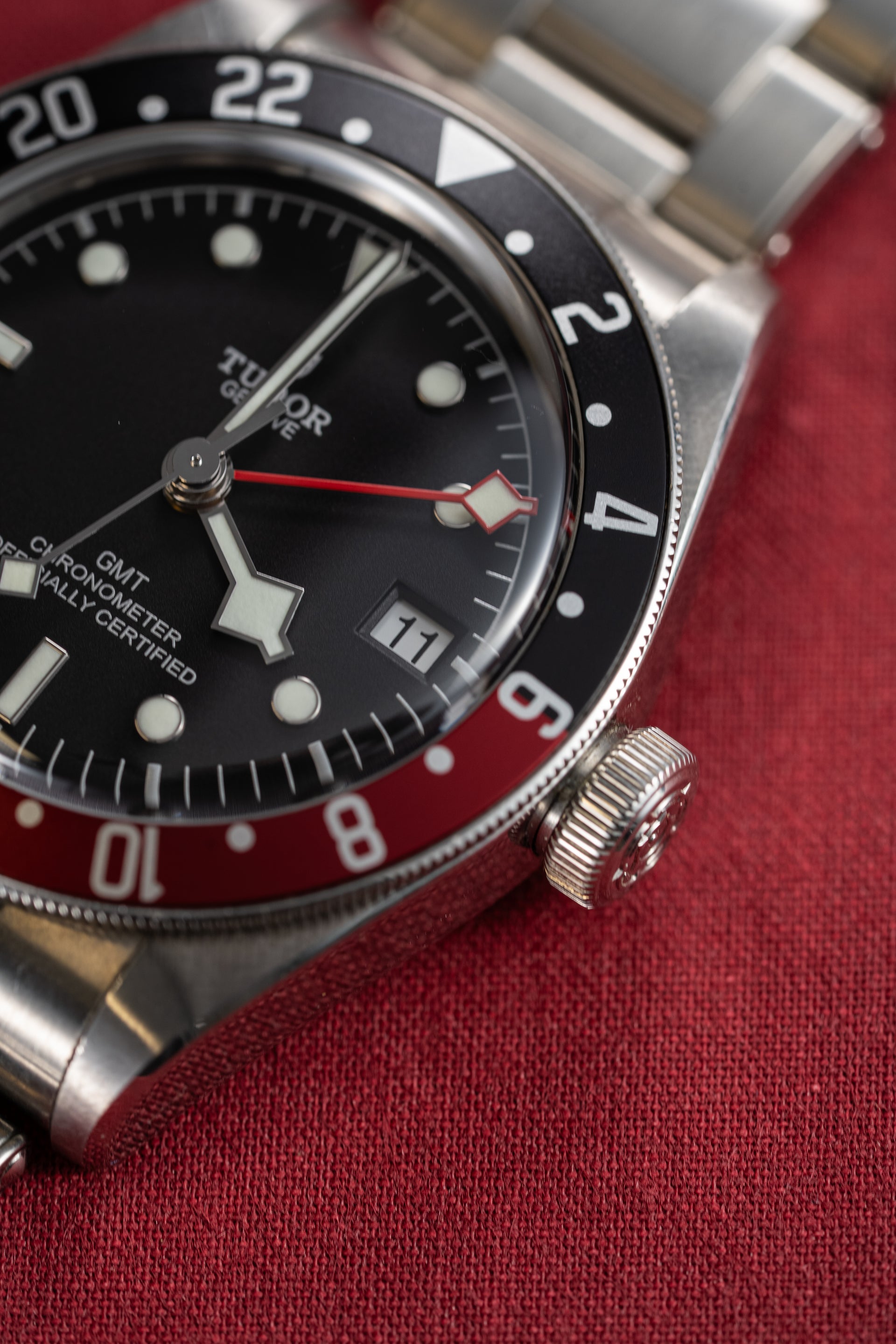 Close-up of a Tudor watch with black dial and red accents on a red fabric background