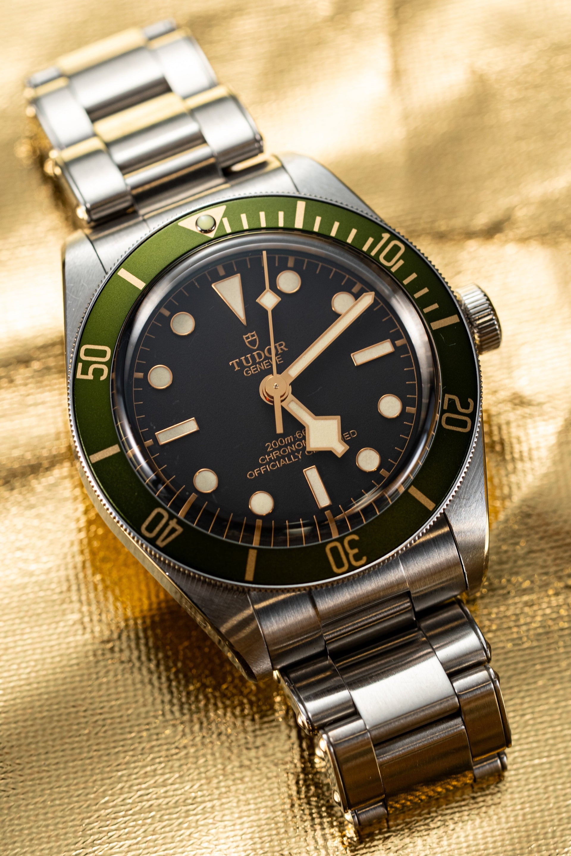 Luxury watch with a silver and green strap on a gold background