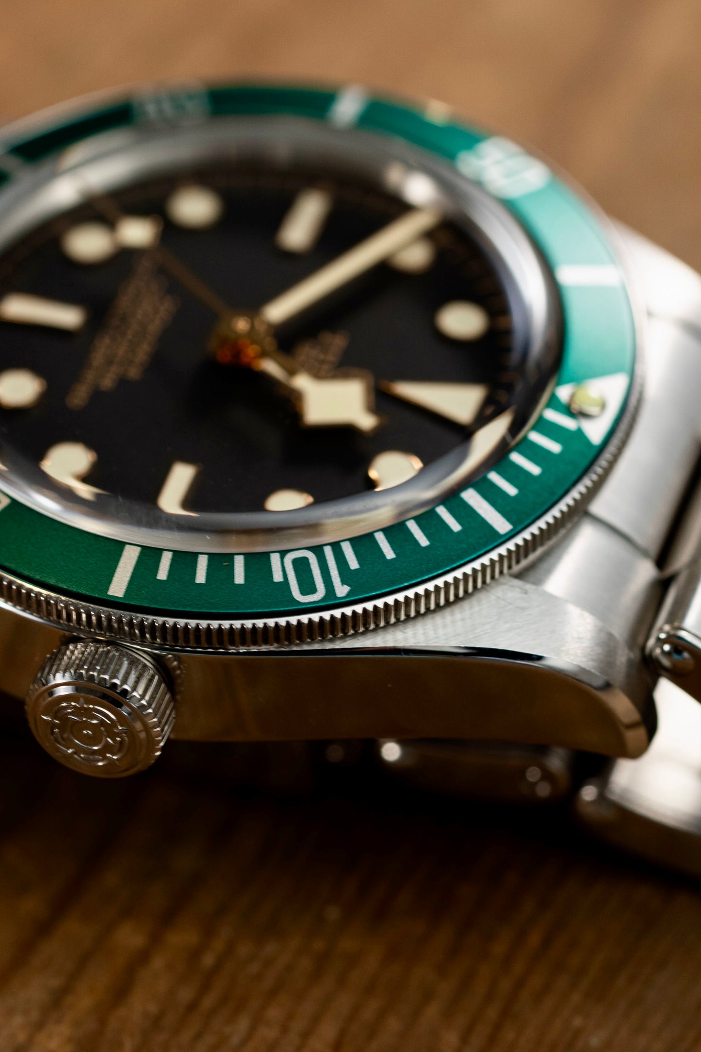 Close-up of a watch with a green bezel and black face on a wooden surface