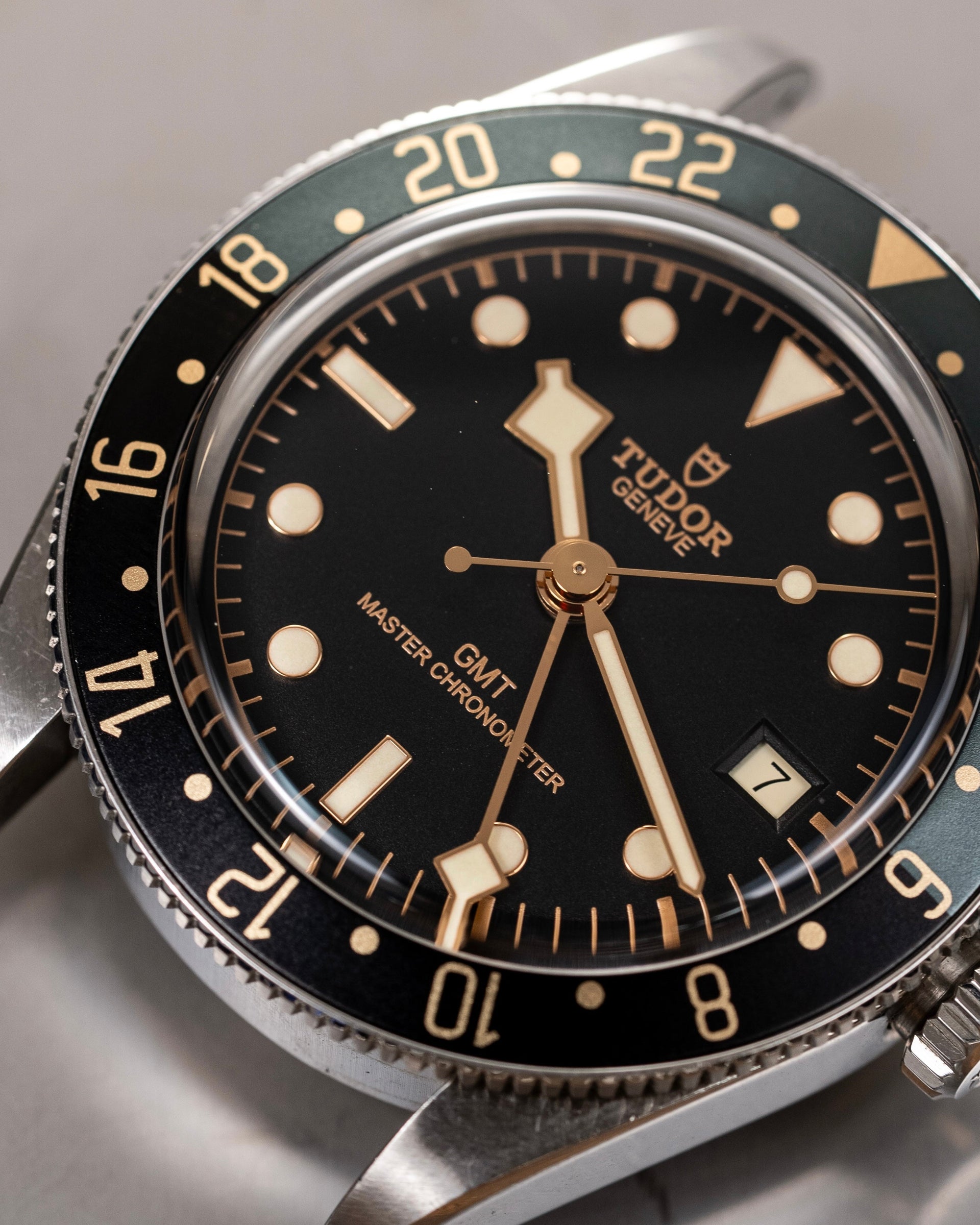 Close-up of a Tudor watch with black dial and silver case on a gray background