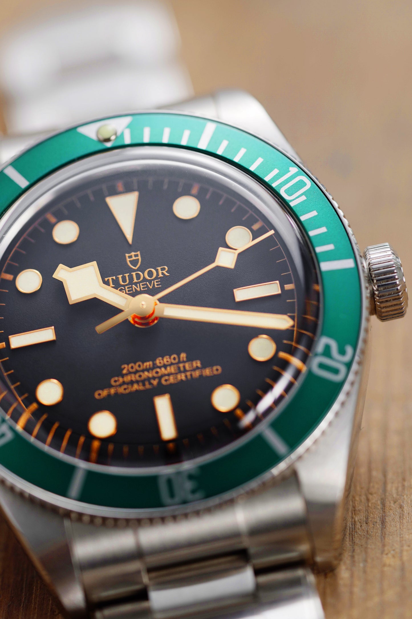 Tudor watch with green bezel and black face on a wooden surface